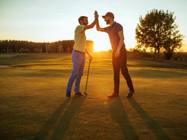 twosome guys on the golf course high fiving at sunset